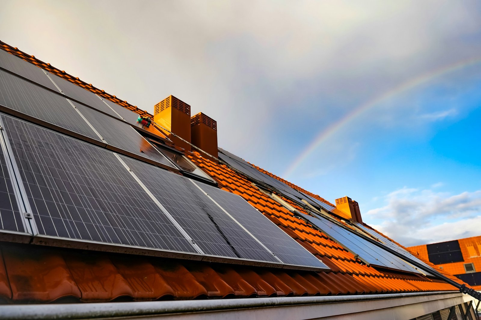 Multiple solar panels on an Aberdeen roof with a rainbow in the background