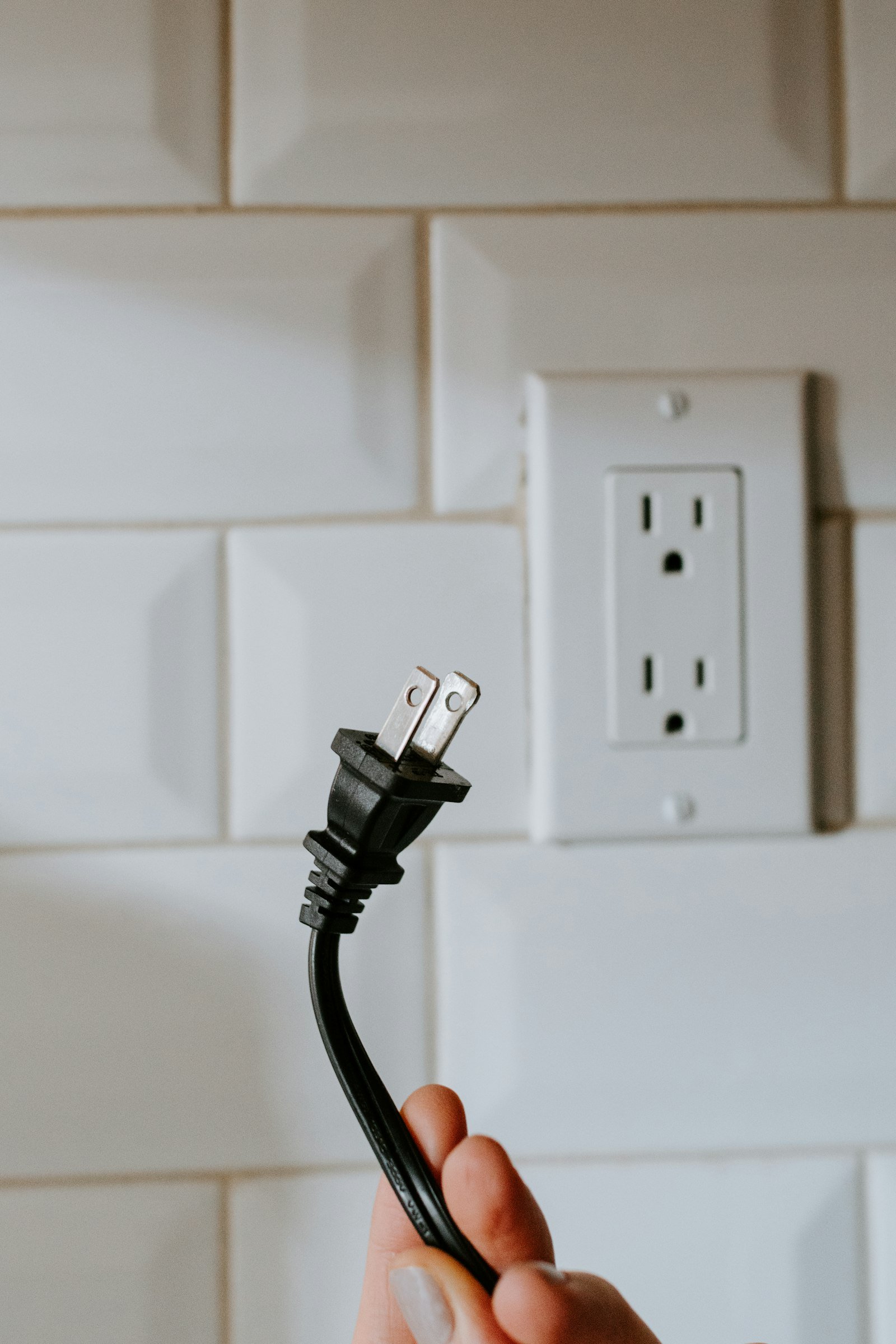 Hand holding plug by tiled wall socket in Maryculter