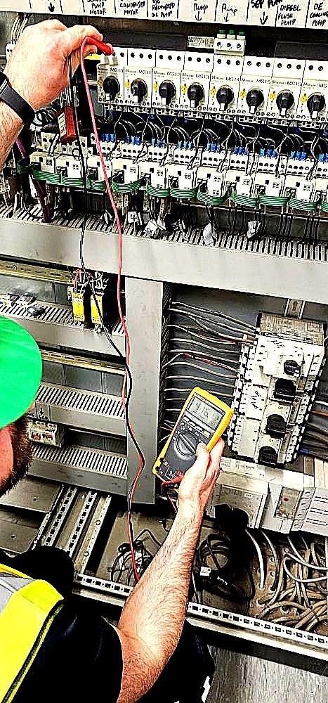EAS qualified electrician testing industrial control panel with Fluke multimeter — UK competence standards October 2026