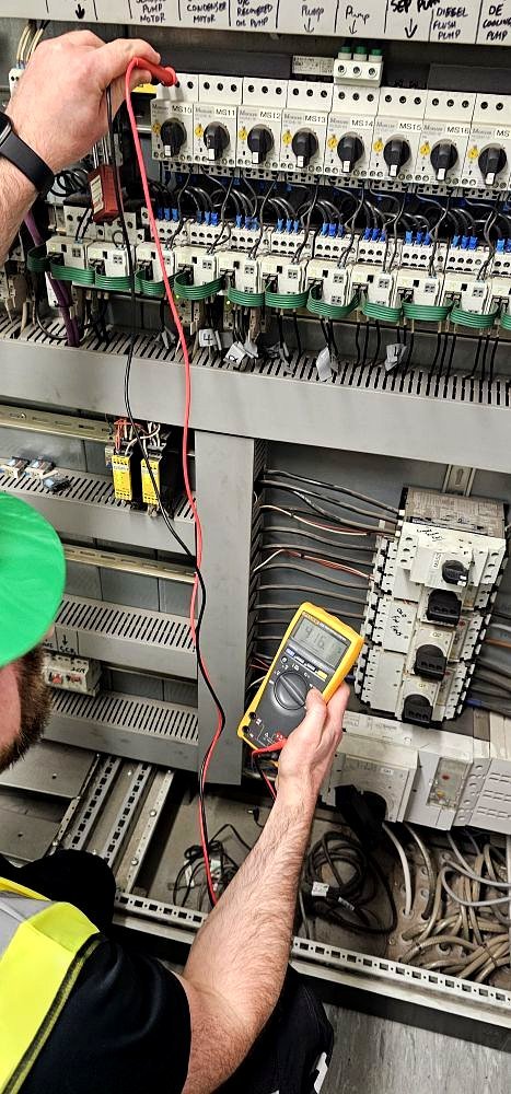 EAS qualified electrician using Fluke multimeter to test industrial control panel — UK competence standards changing October 2026