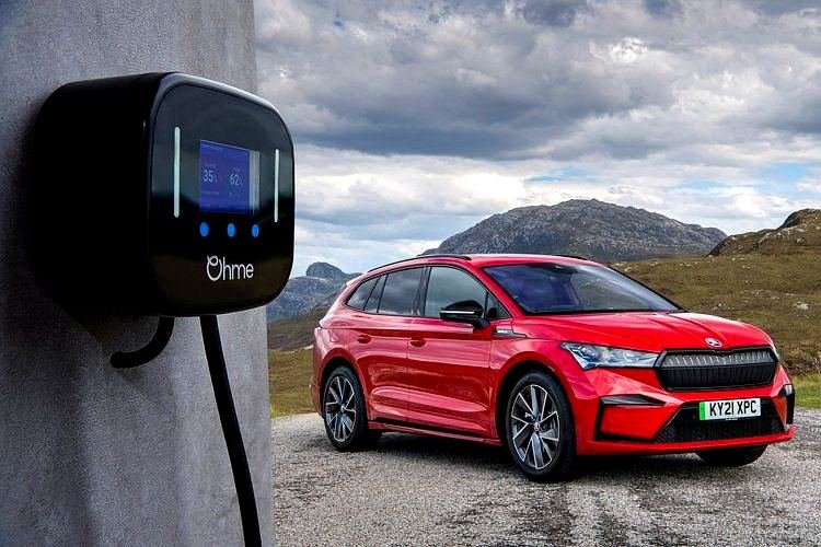 Ohme Home Pro EV charger installed on grey rendered wall with dramatic Scottish mountain backdrop and red Skoda Enyaq