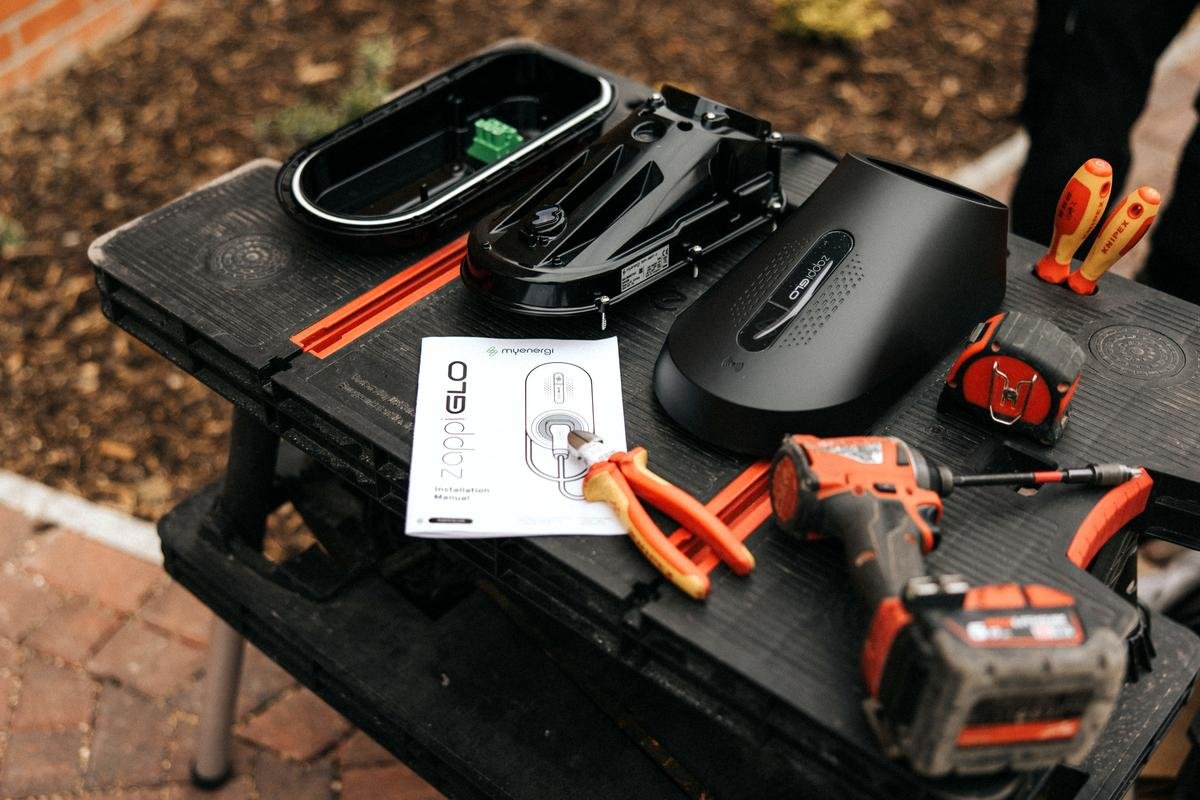 zappi GLO EV charger components laid out with myenergi installation manual and electrician tools