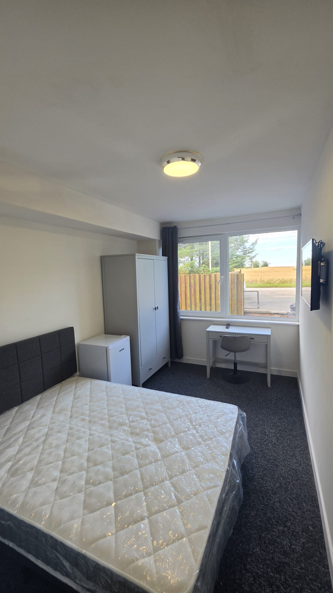 Letting room in a Peterhead accommodation conversion with a ceiling light, a desk under the window and a wall mounted television
