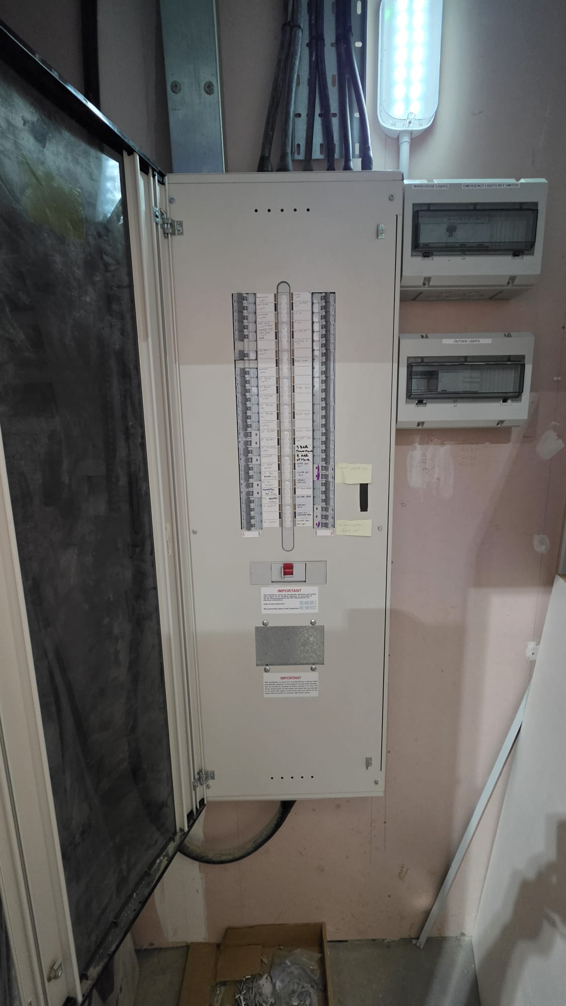 Three phase distribution board in an Aberdeen warehouse plant room with an inspection label and separate boards for warehouse lights and emergency lighting