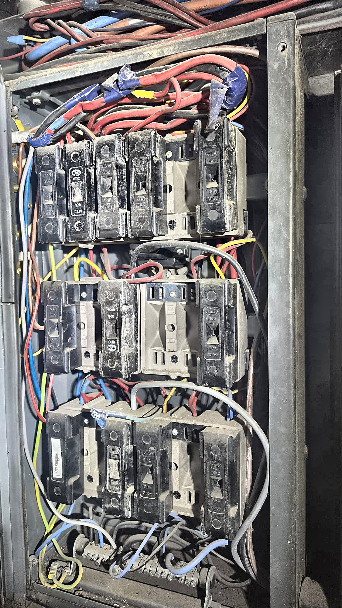Old HRC fuse carriers with mixed cable colours and taped joints in a steel cabinet, found during an industrial EICR in Aberdeen