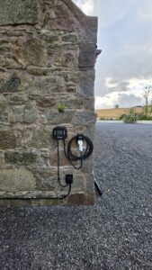 Ohme EV charger on a granite stone wall at a gravel driveway in Ellon, with the tethered cable coiled on its holder