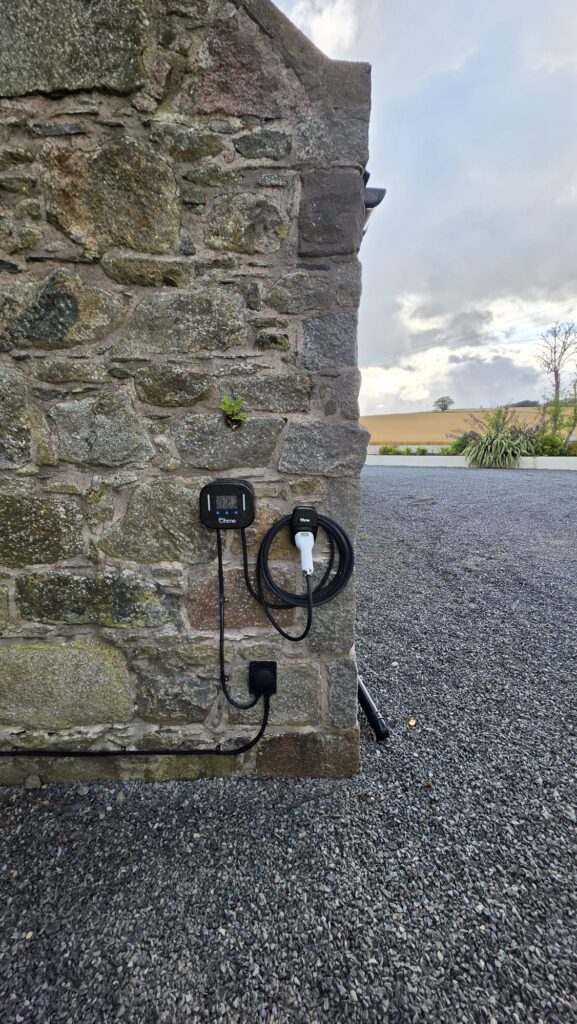 Ohme EV charger on a granite stone wall at a gravel driveway in Ellon, with the tethered cable coiled on its holder