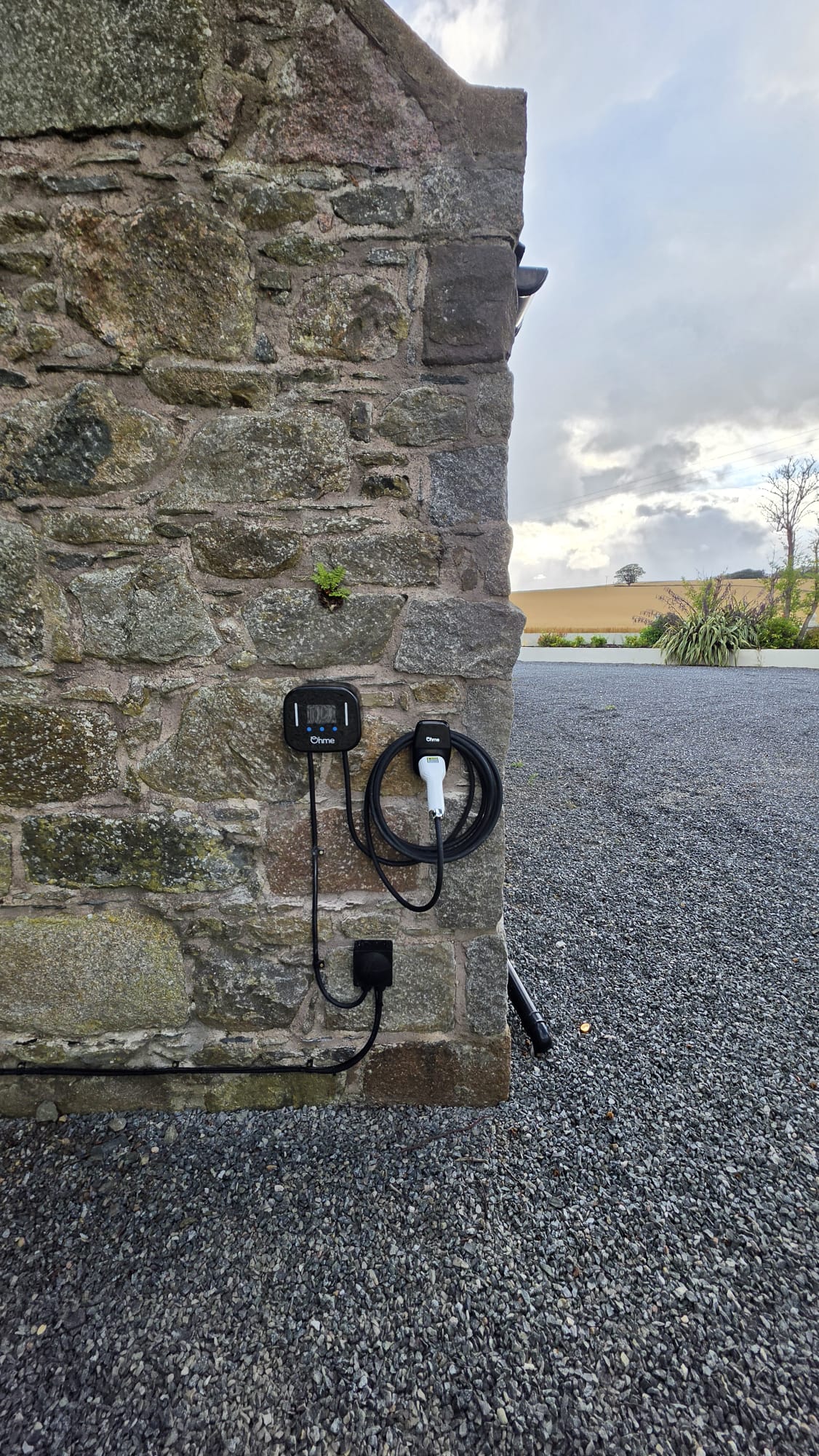 Ohme EV charger we fitted on a granite stone wall in Ellon, with the tethered cable coiled on its holder