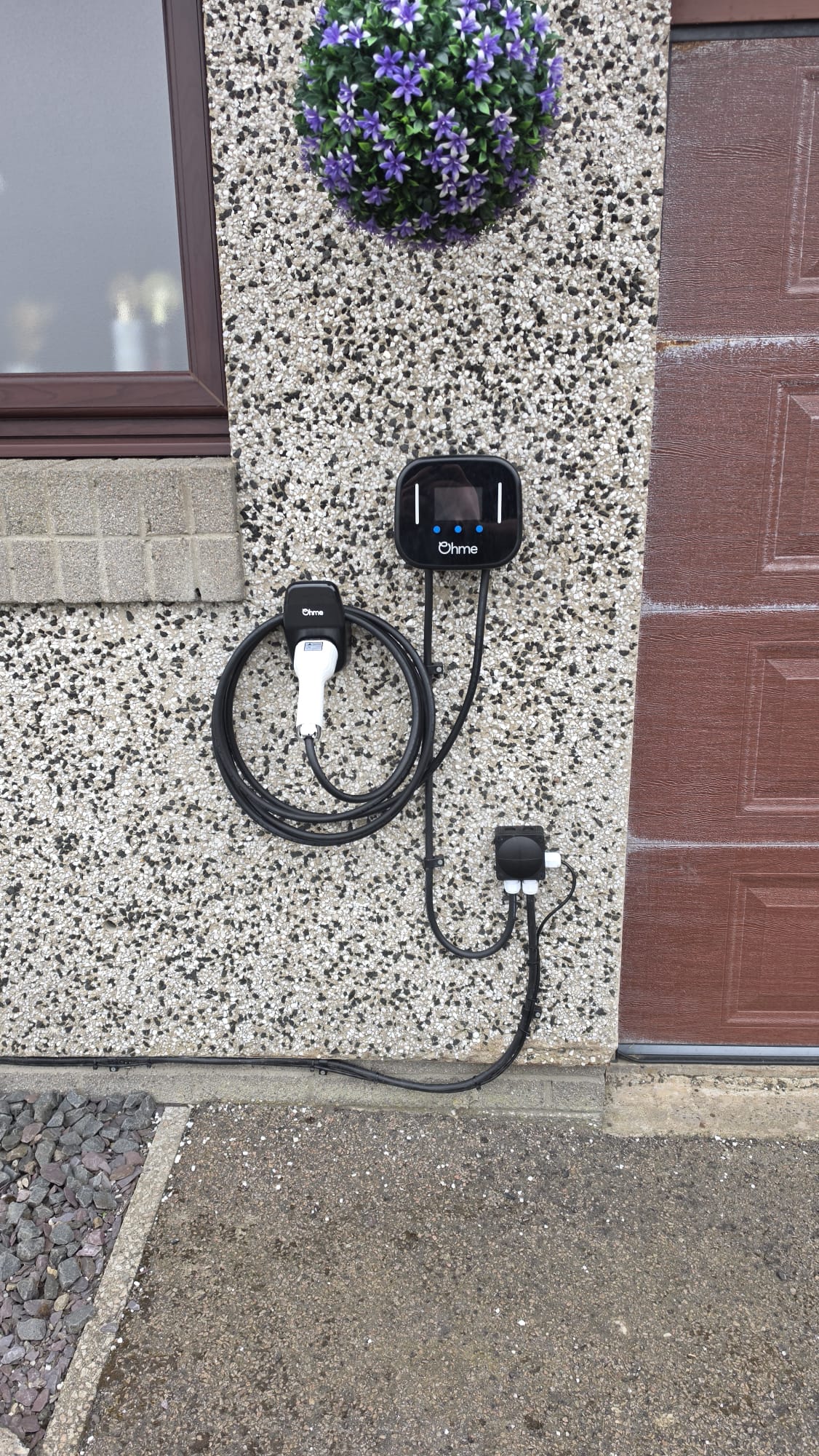Ohme EV charger fitted to speckled pebbledash beside a brown garage door in Peterhead with the cable run clipped