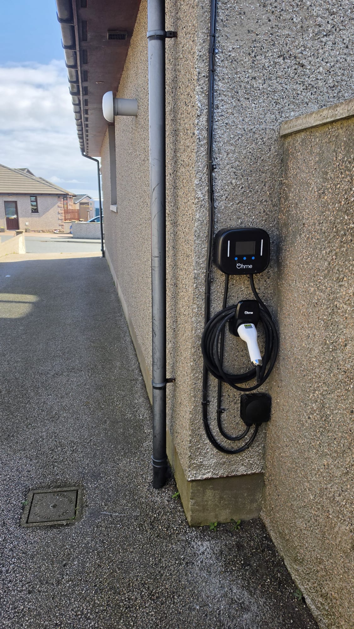 Ohme EV charger with its cable routed neatly down a pebbledash wall in a side passage in Peterhead