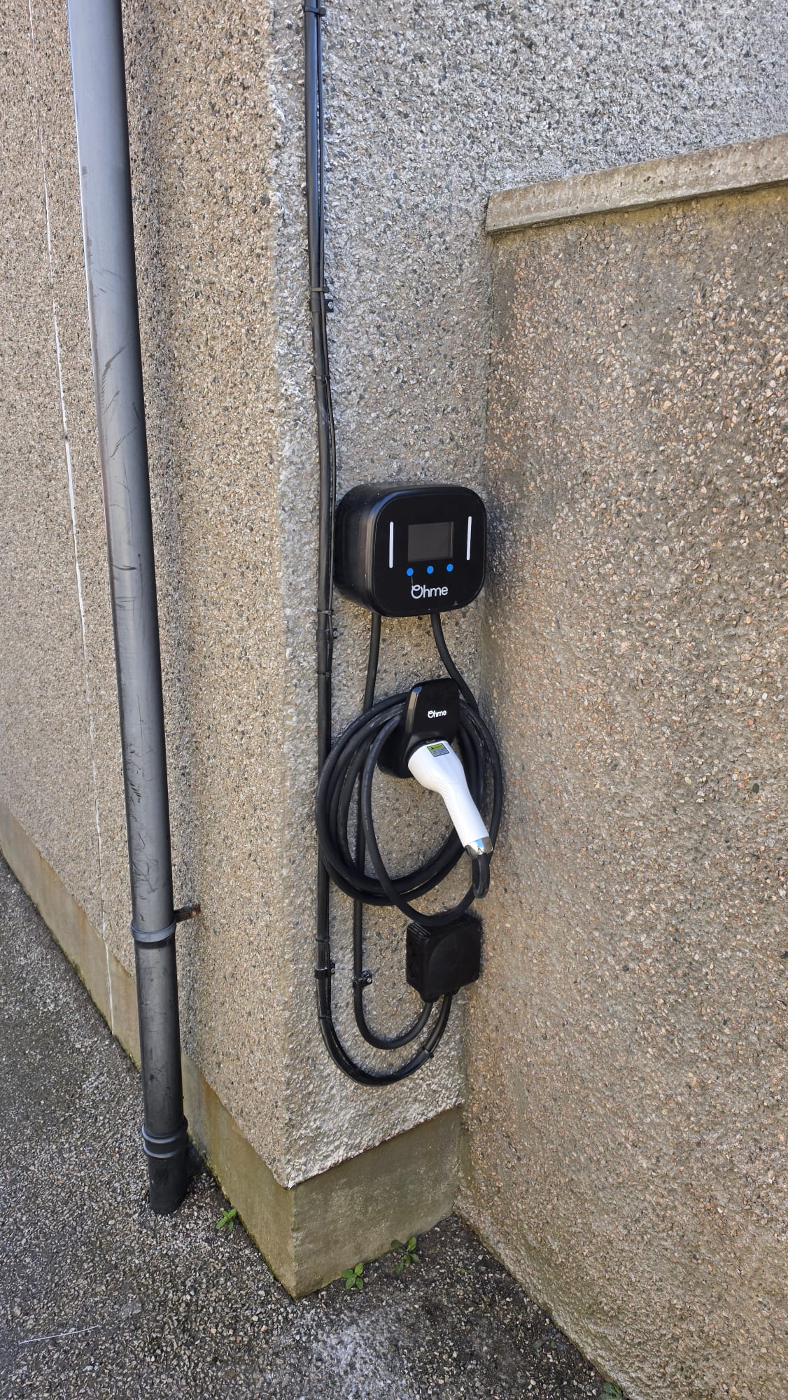 Wall mounted Ohme EV charger with its tethered cable coiled on the holder in Peterhead